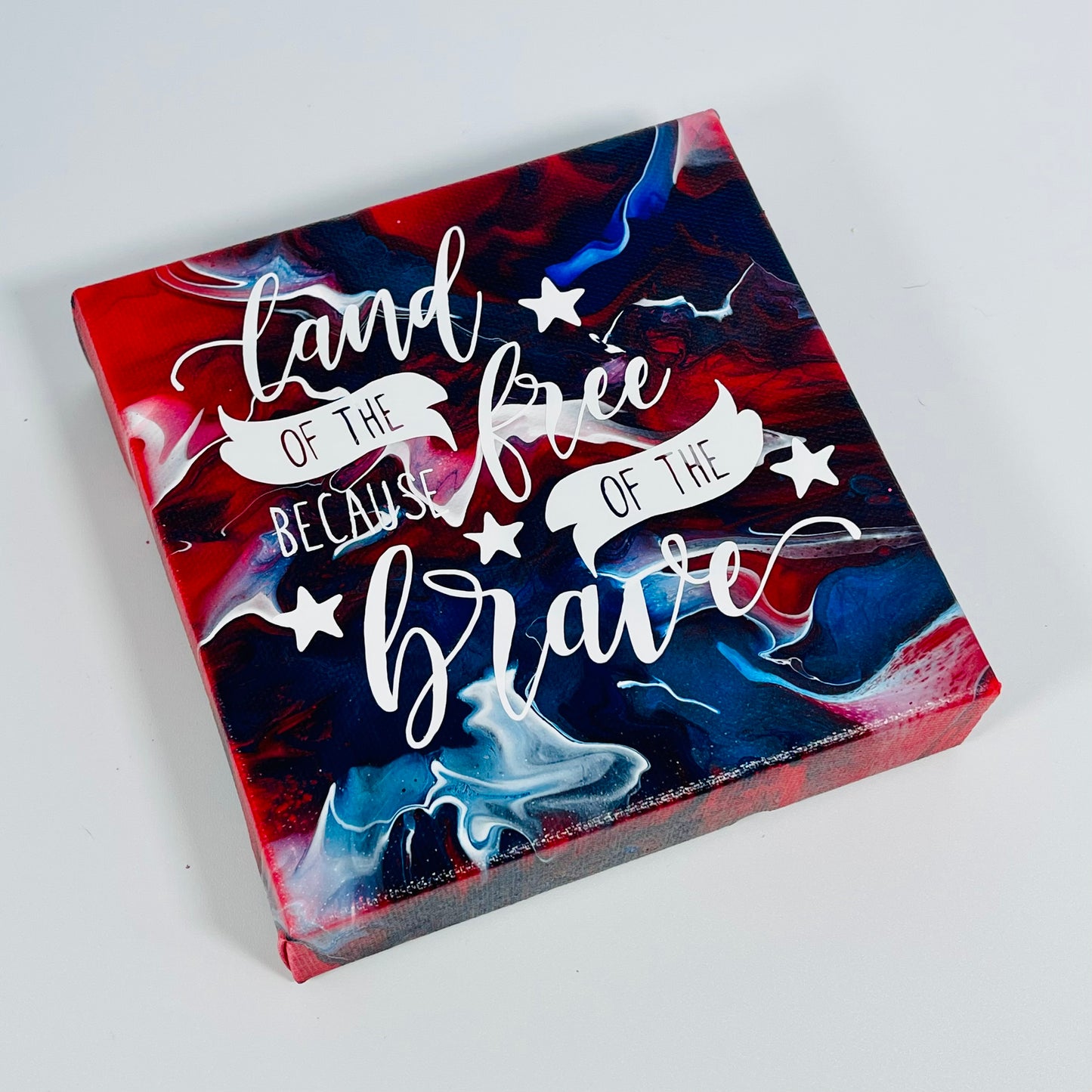 The Banner Freedom Block. A red, white, and blue hand painted painting that says 'land of the free because of the brave'