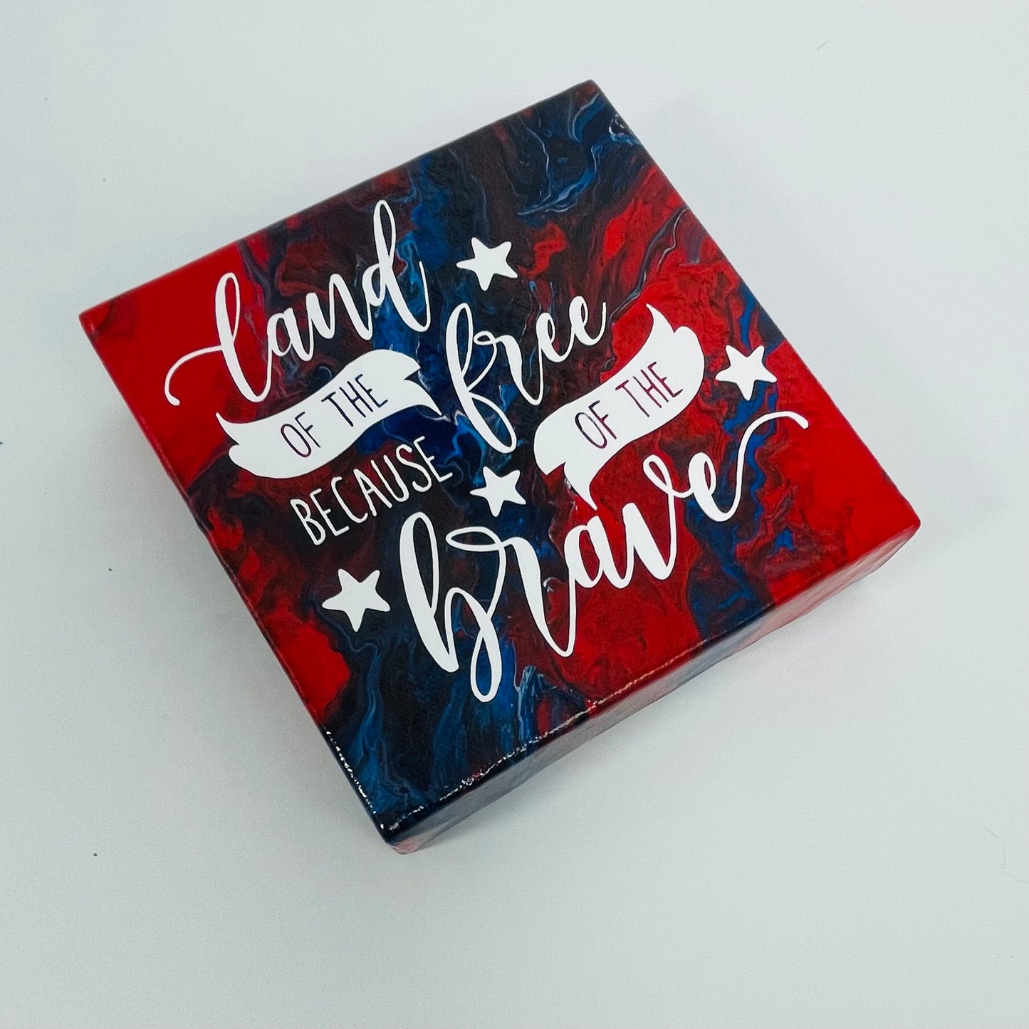 The Colonel Freedom Block. A red, white, and blue hand painted painting that says 'land of the free because of the brave'