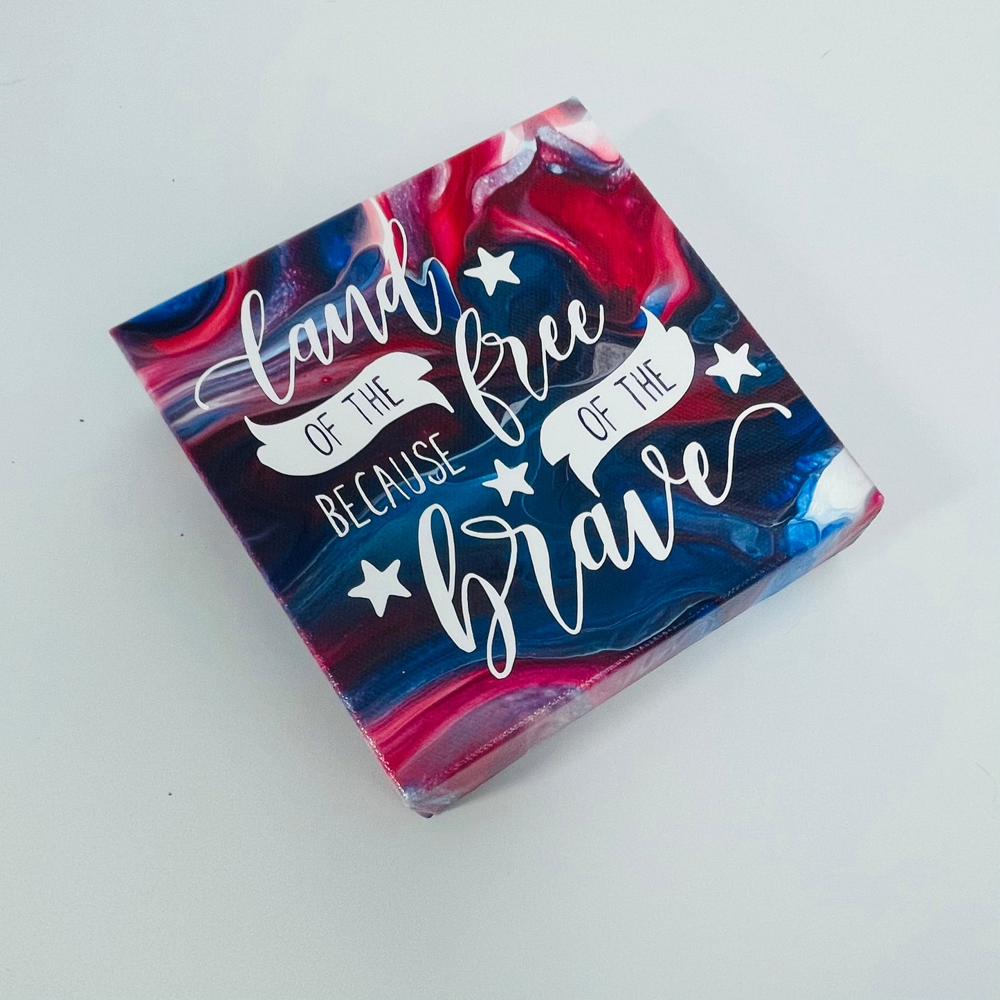 The Commander Freedom Block. A red, white, and blue hand painted painting that says 'land of the free because of the brave'