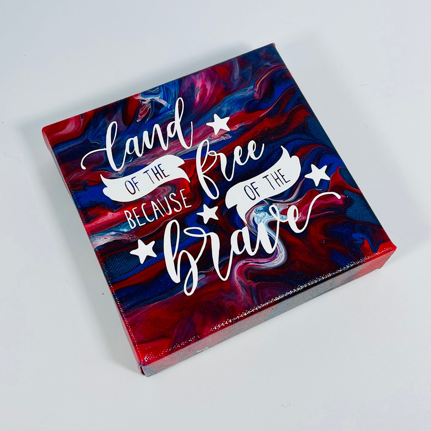 The Indy Freedom Block. A red, white, and blue hand painted painting that says 'land of the free because of the brave'