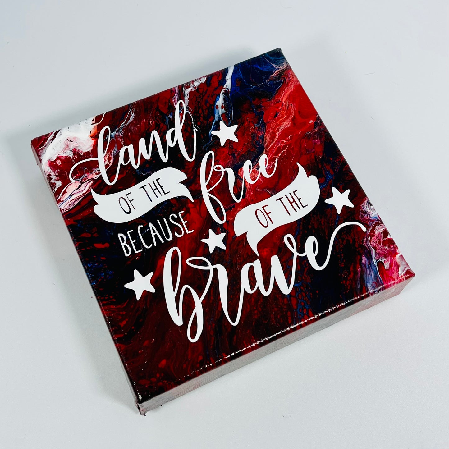 The July Freedom Block. A red, white, and blue hand painted painting that says 'land of the free because of the brave'