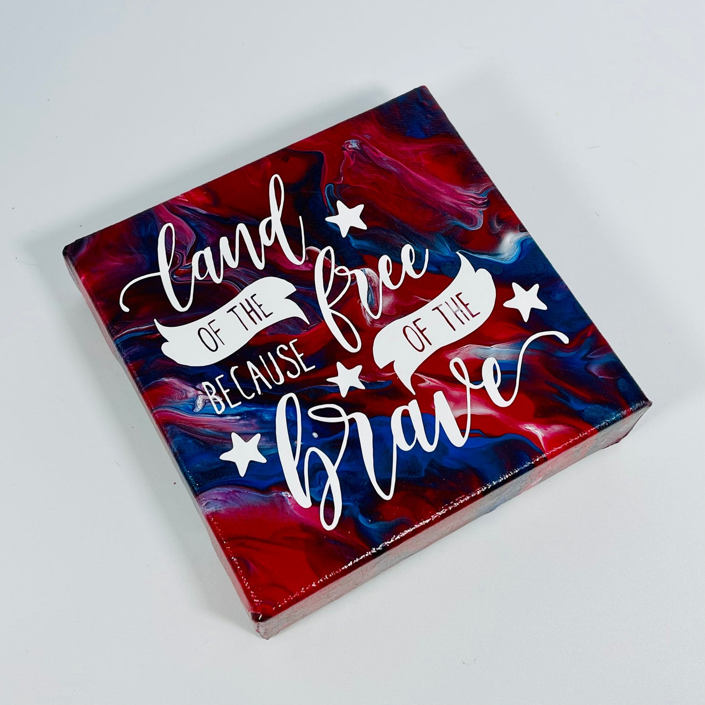 The Peace Freedom Block. A red, white, and blue hand painted painting that says 'land of the free because of the brave'